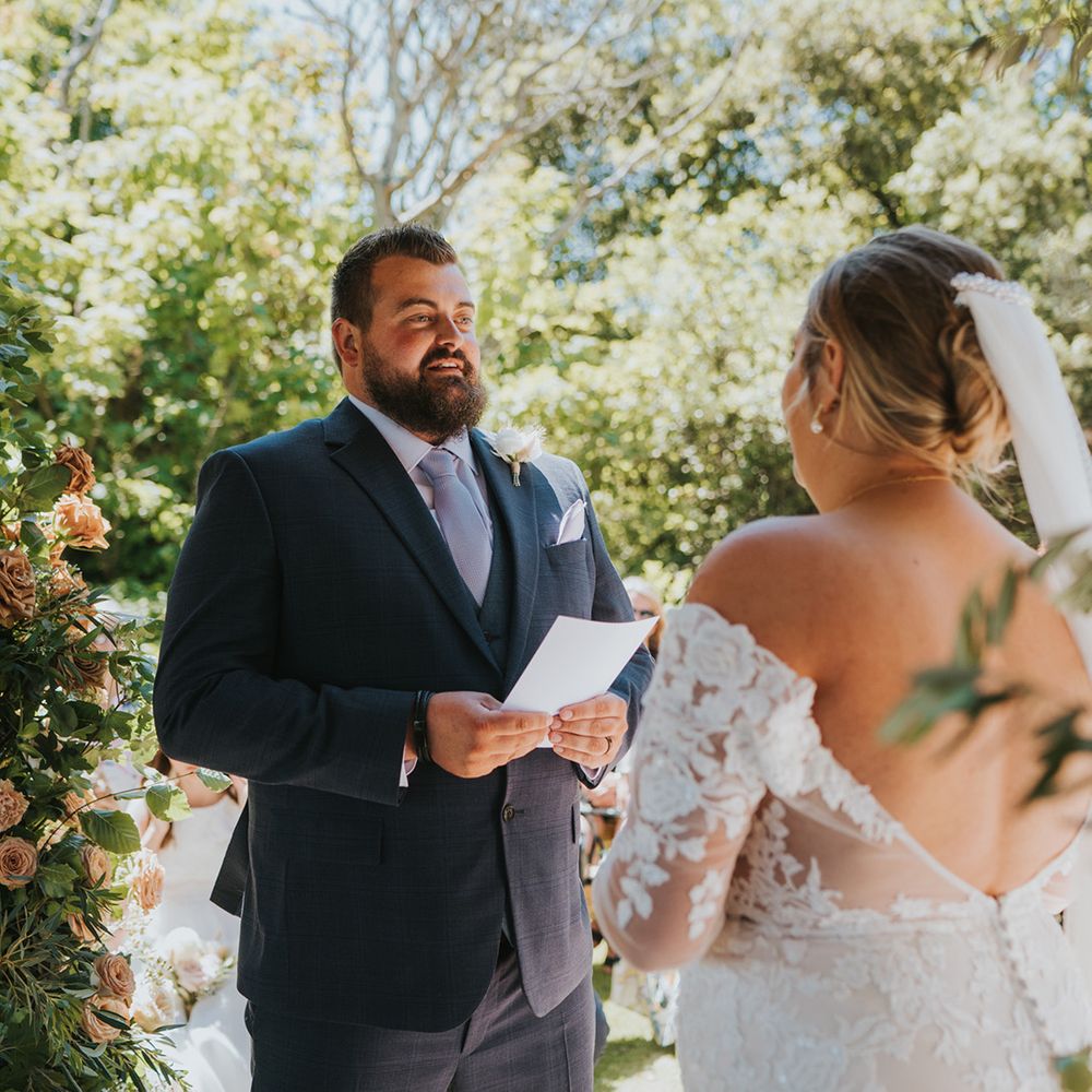 Groom reads wedding vows during ceremony outdoors beneath pergola 