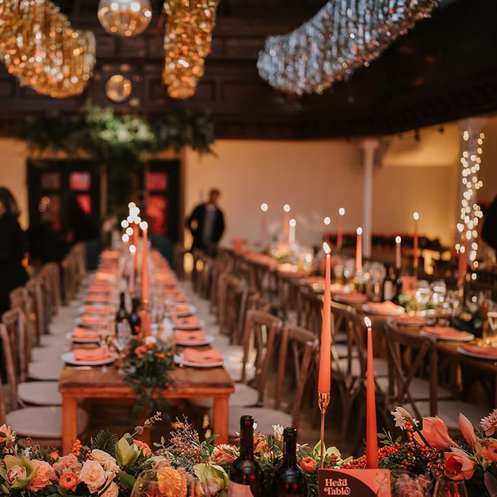 Head table of Christmas multicultural London wedding with streamer decorations, orange flower and foliage table runners, orange tapered candles and suspended foliage decor