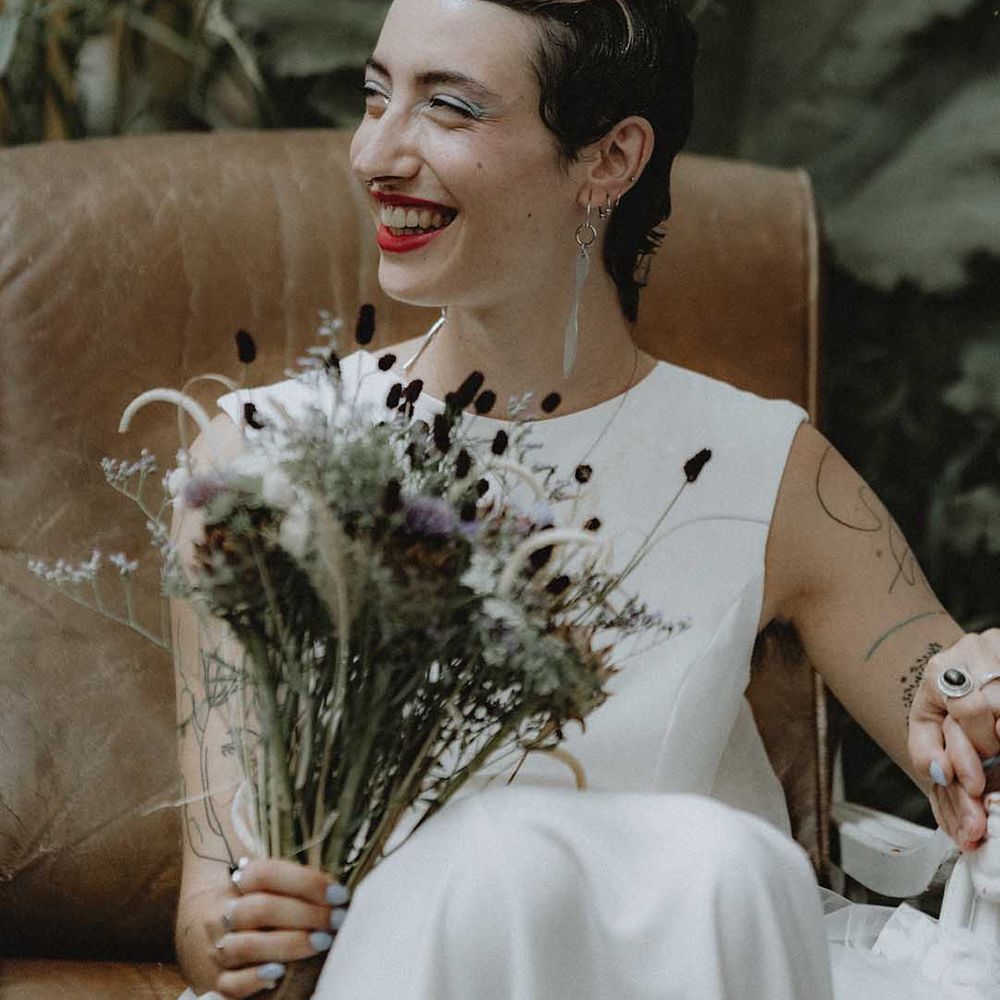 Lisa wears red lipstick and dark hair slicked back into 20s styling complete with DIY bridal bouquet 