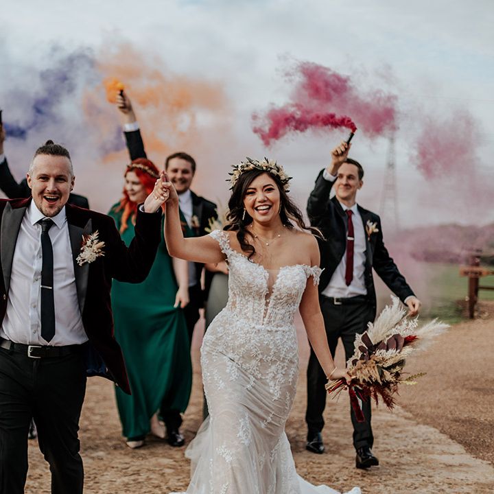 Smoke bomb wedding portrait with the bride and groom and their wedding party in burgundy and green wedding outfits 