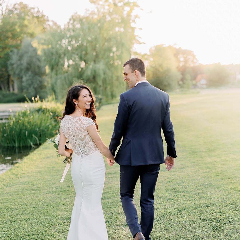 bride in a lace back Kelly Faetanini fitted wedding dress holding hands with her groom in a navy suit