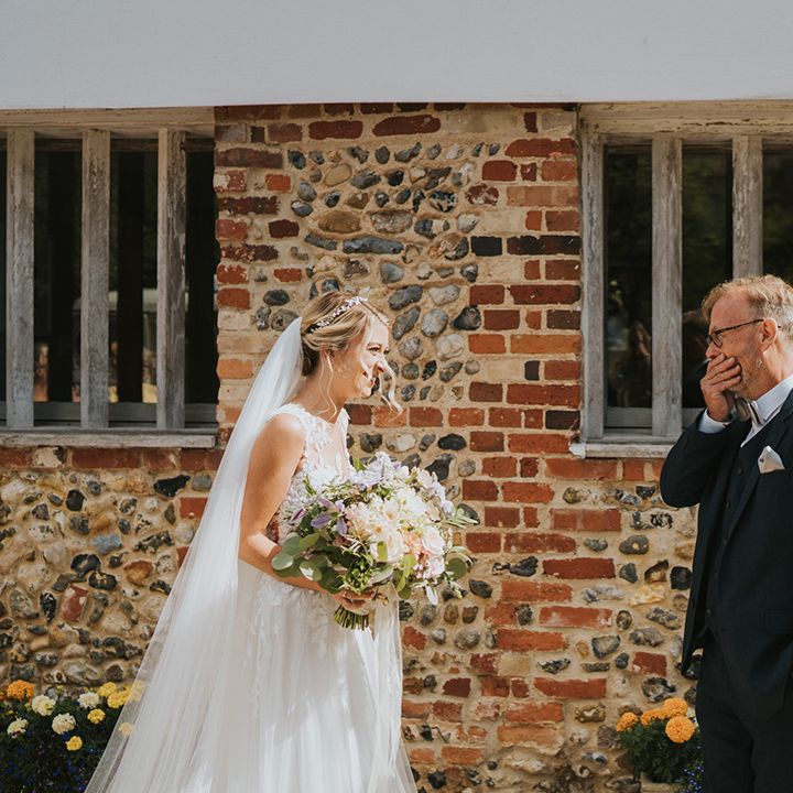 Father of the bride in a navy suit and silver bow tie gets emotional as he sees the bride in her wedding dress for the first time 