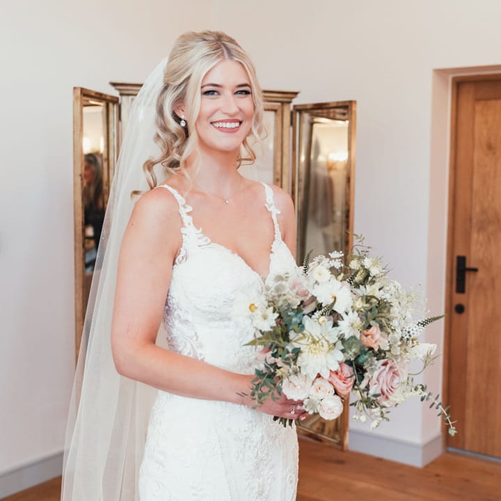 Bride in fitted lace wedding dress and veil with her blonde hair in a half up half down hairstyle with all white wedding bouquet 
