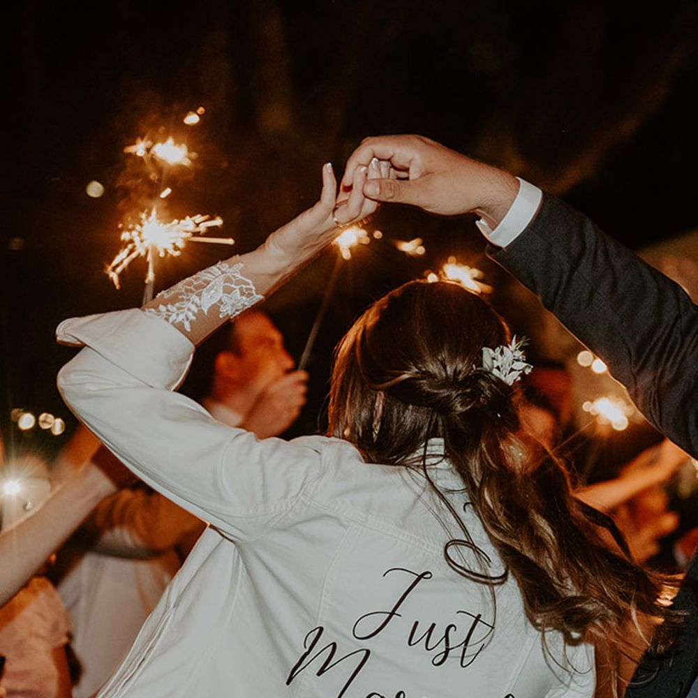 The groom twirls the bride who wears a white denim jacket with black font reading 'Just Married'