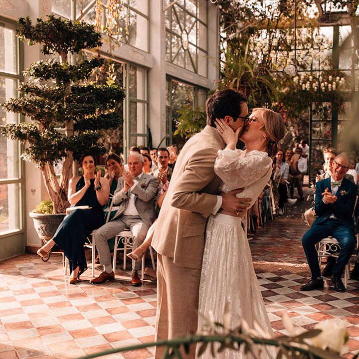 Glass house wedding venue with the bride and groom sharing their first kiss as a married couple 