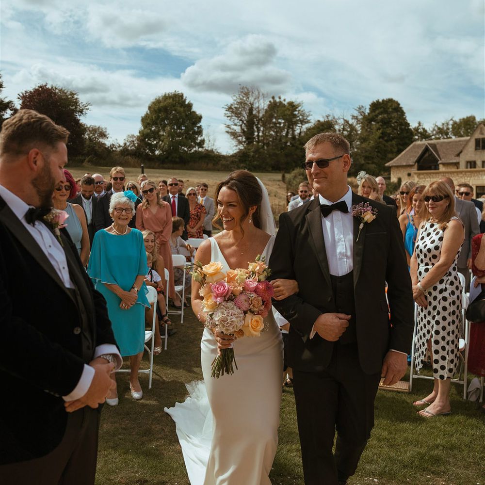Bride holding colourful pink and orange rose and gypsophila bouquet walking down the aisle with her father 