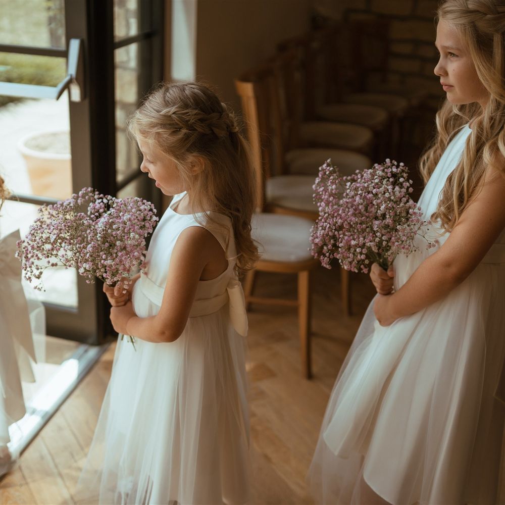 Flower girls in pretty white dresses tied with bows holding bouquets of gypsophila 