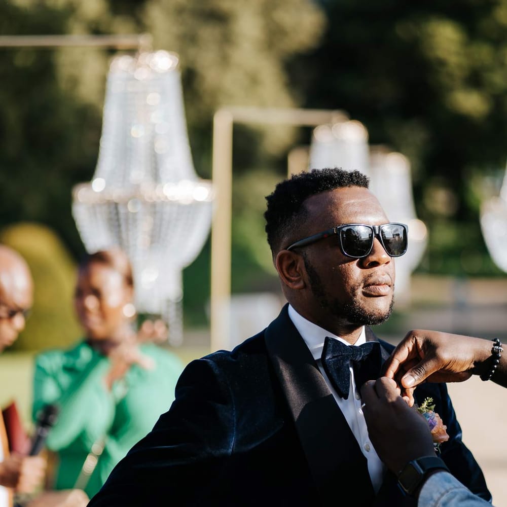 Groom in velvet midnight blue double breasted groom’s blazer, velvet bowtie, peach garden rose boutonniere and sunglasses 