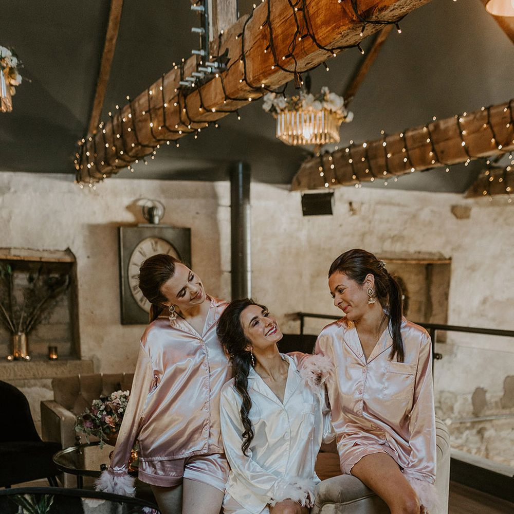 Bridesmaids in pink satin pyjamas with the bride in white pyjamas on the morning of the wedding 