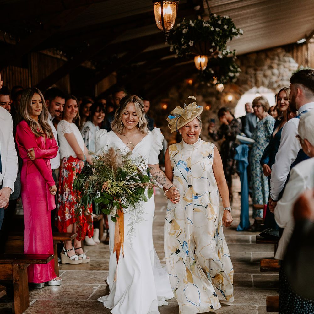 Mother of the bride in a patterned wedding outfit walks the bride down the aisle 