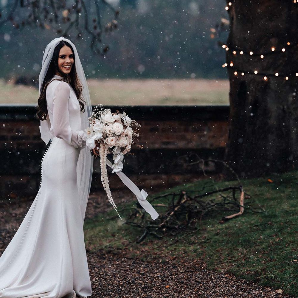 Bride in satin long sleeve wedding dress at Iscoyd Park for winter wedding carrying white flower bouquet