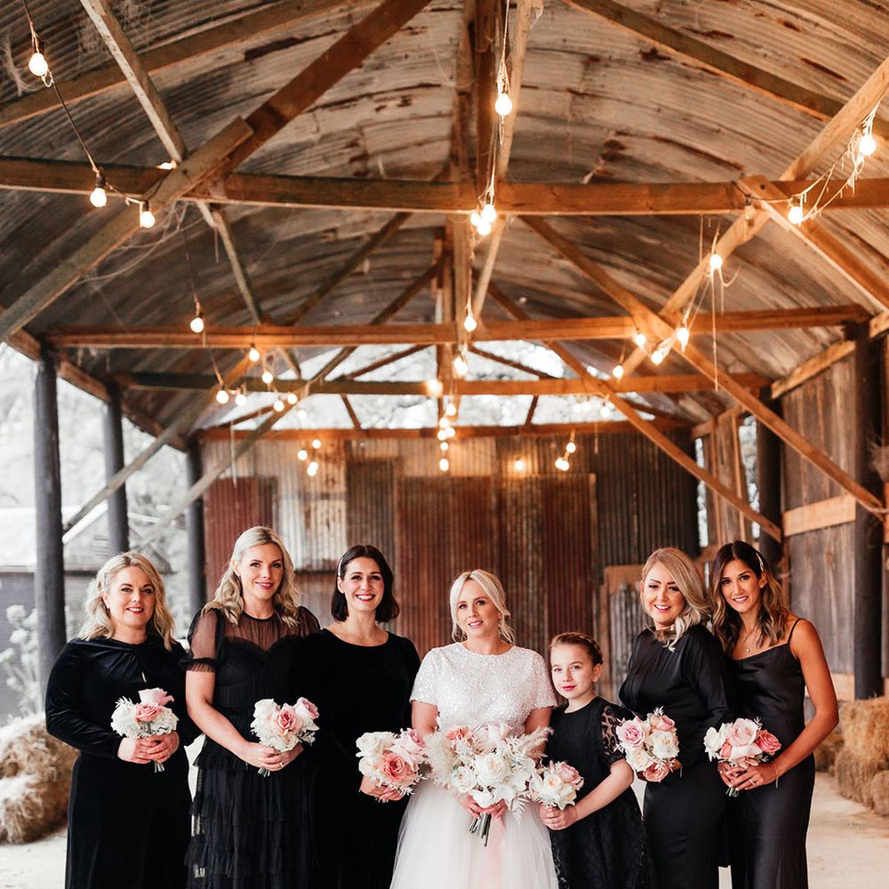 Bride standing with bridesmaids in black bridesmaid dresses in rustic barn winter wedding venue 