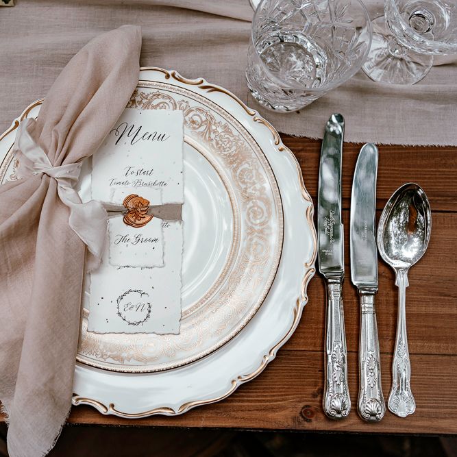Place setting with vintage plates and cutlery, natural linen napkin and recycled paper menu card