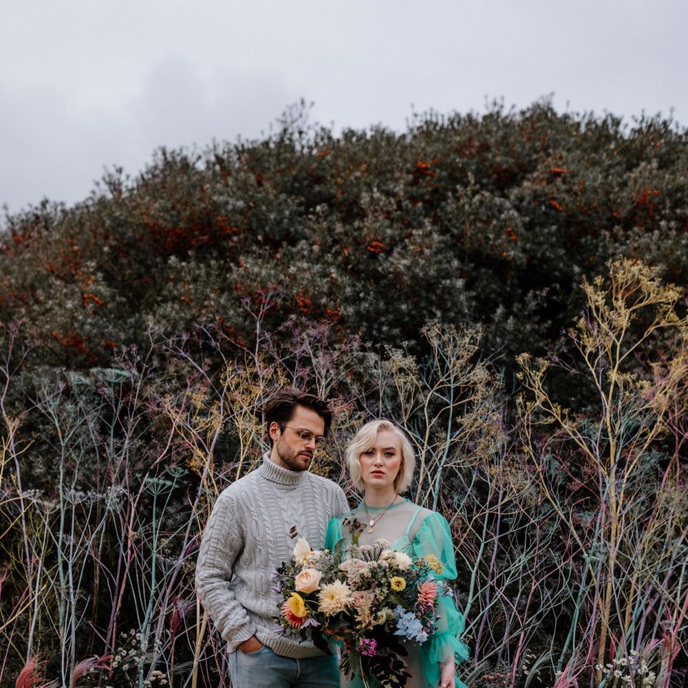 Contemporary couple at a colourful beach elopement with the bride in a sheer green wedding dress and the groom in a wooly jumper