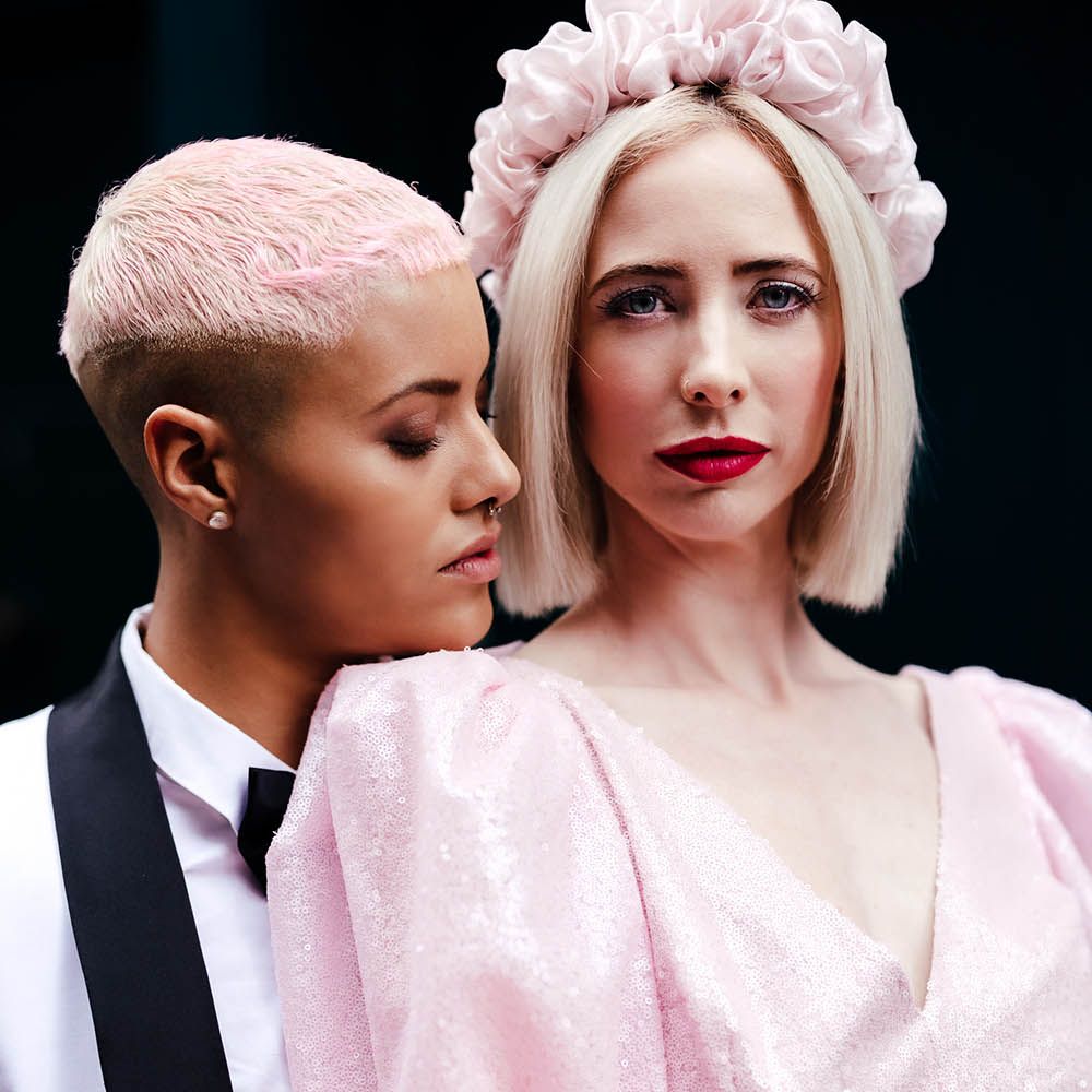 Bride with short pink hair embracing her bride in a pink jumpsuit with blonde bobbed hair and red lipstick 