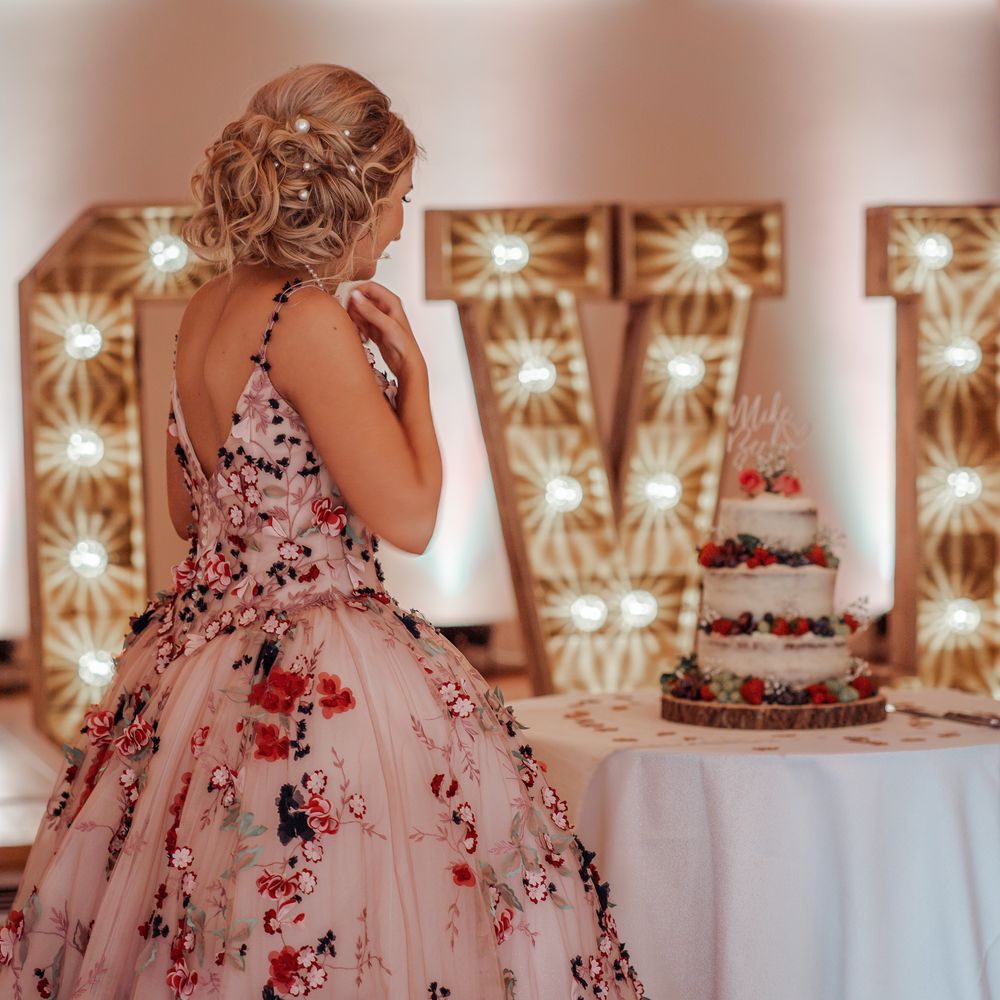 Bride stands in front of LOVE wedding sign with lights 