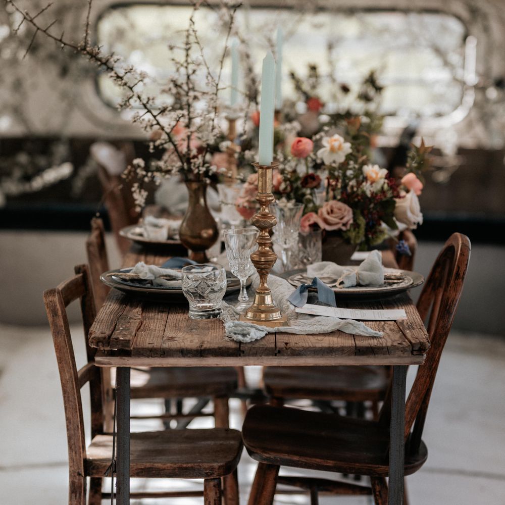 Wooden rustic table with brass candleholders and pastel florals and pale blue napkins
