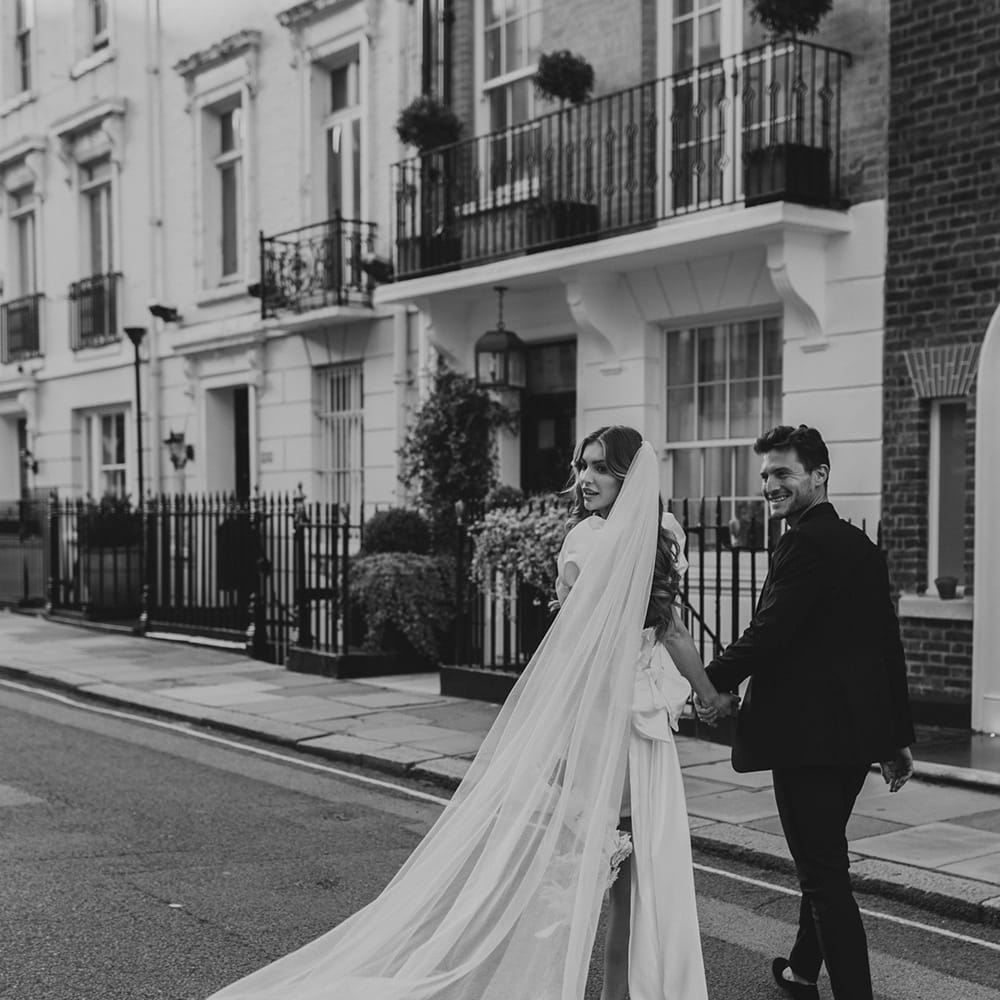 Black and white portrait of a bride in a short wedding dress with her long wedding veil billowing in the wind 