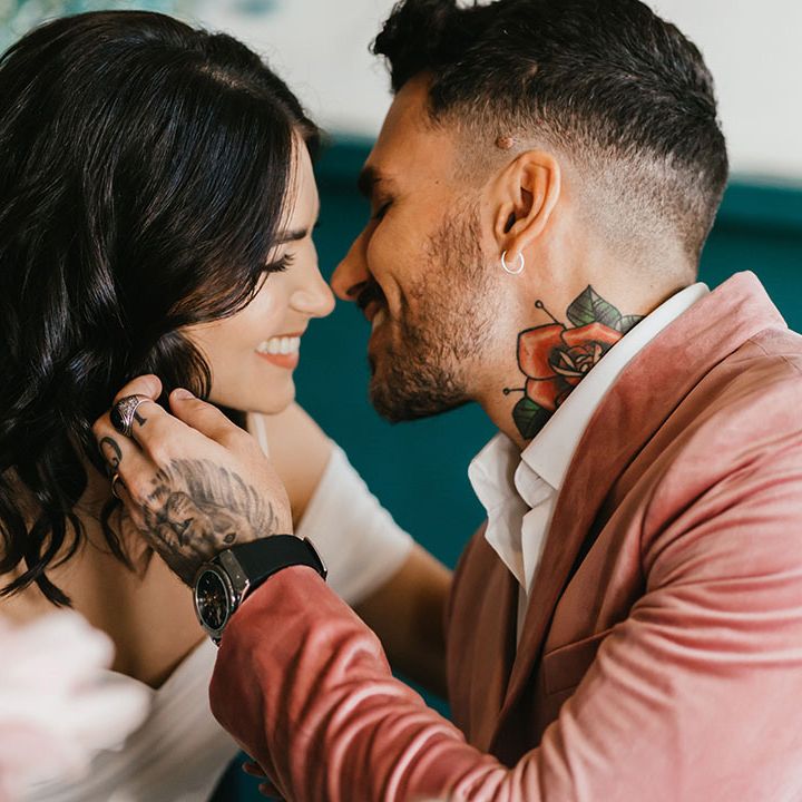 Groom in a pink velvet jacket kissing his bride with short curly hair at their city wedding 