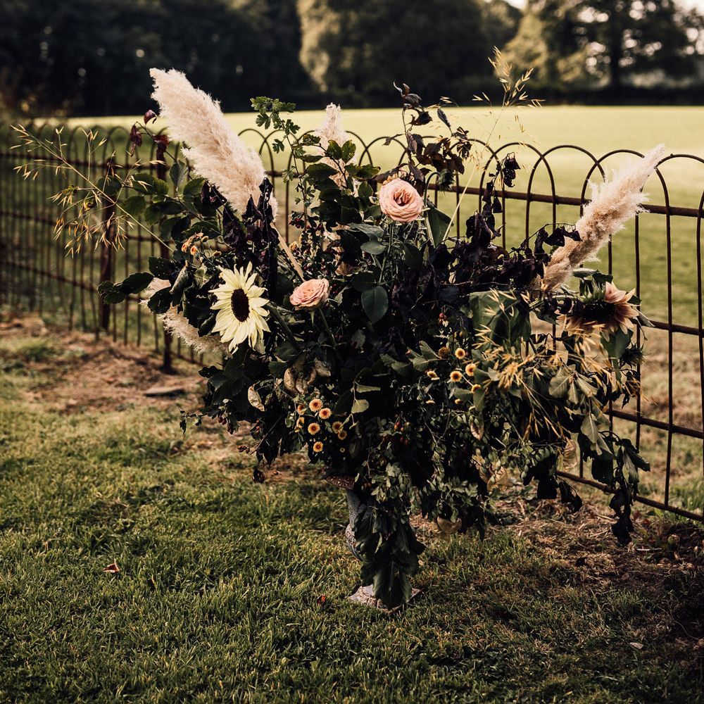 Floral installation in garden with foliage, roses, pampas grass and sunflowers for garden wedding reception in Cornwall