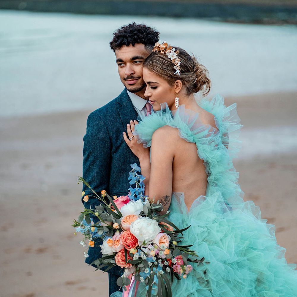 Bride in a mint green tulle wedding dress embracing her husband in a blue wool suit at their pastel beach elopement 