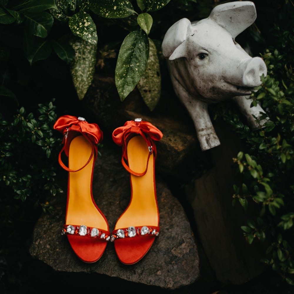 Red heeled sandals with gem encrusted straps and bows placed on rock for The Wellbeing Farm wedding in Lancashire