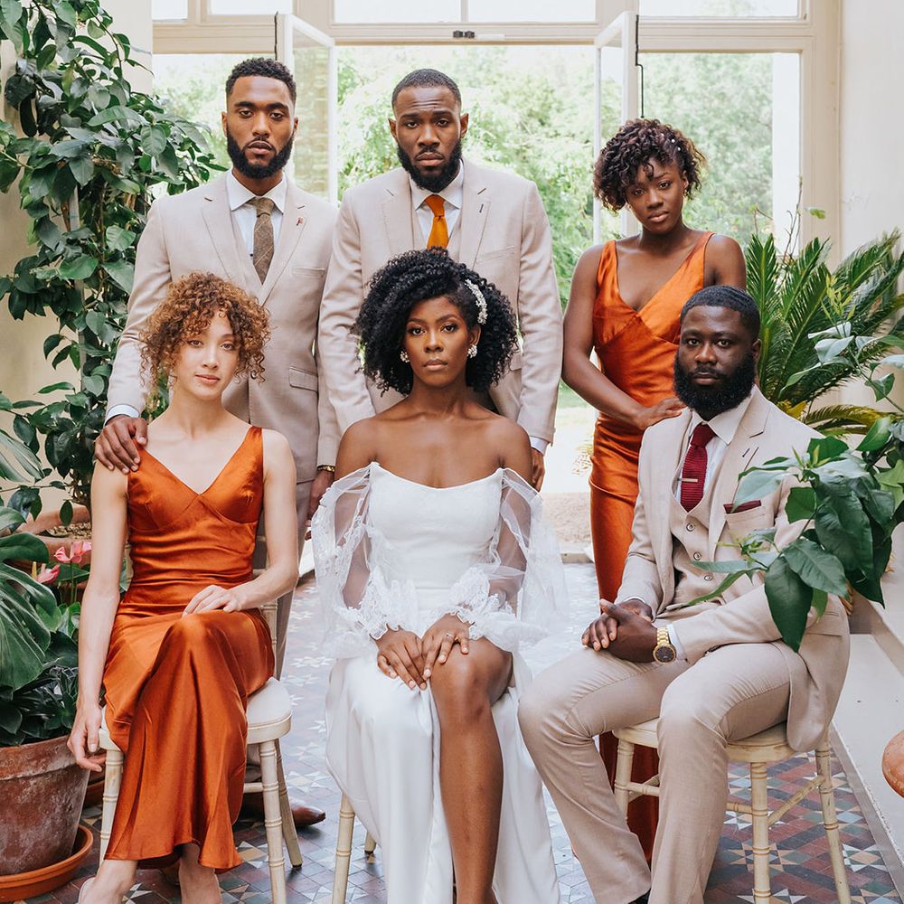 Stylish wedding party in orange satin bridesmaid dresses, beige suits and a strapless wedding dress with side slit