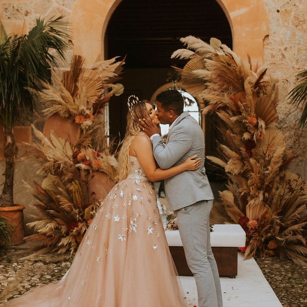 Bride & groom kiss on their wedding day in front of pampas grass installations for wedding in Mallorca 