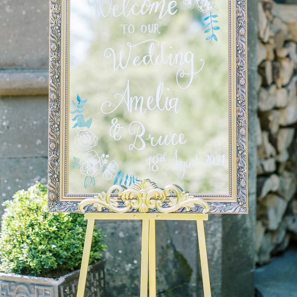 Wedding welcome sign made from a gold guilt mirror on an easel with white calligraphy 
