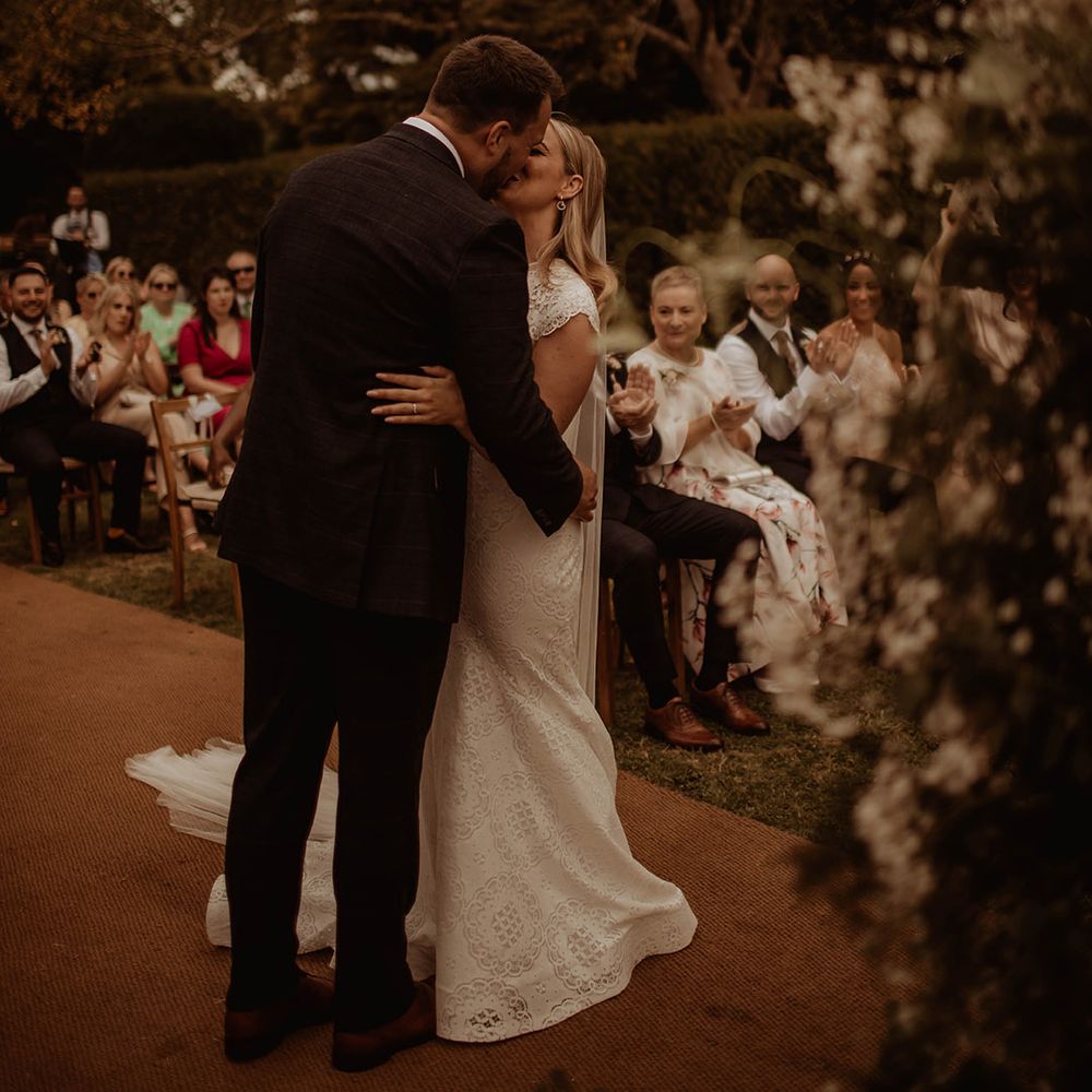 Groom kissing his bride in a lace wedding dress at their outdoor Dewsall Court wedding 