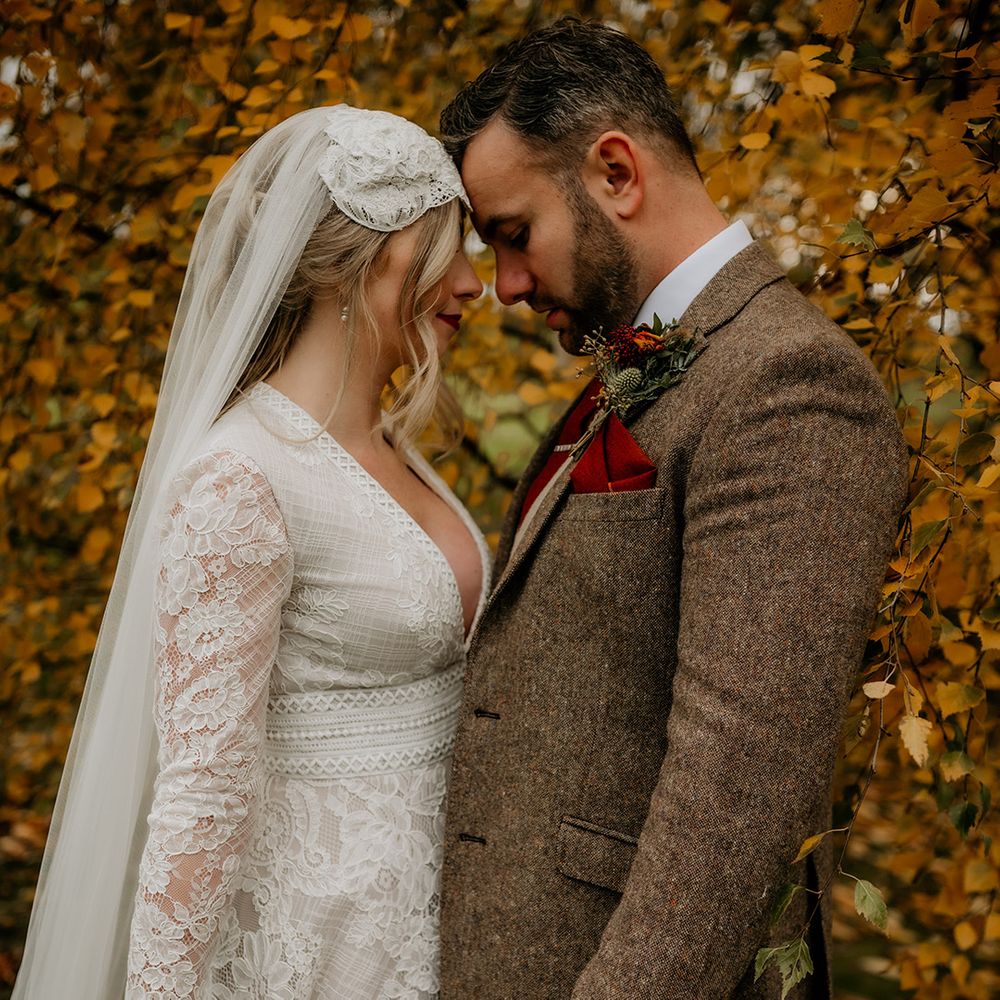 Bride and groom autumn wedding photograph with bride in a lace wedding dress with long sleeves and groom in a tweed suit 