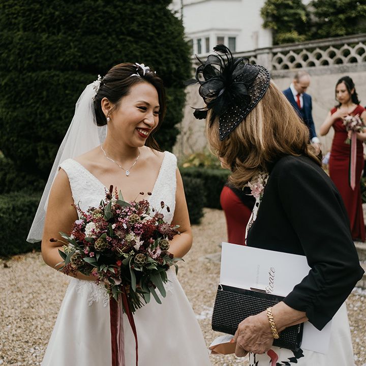 Bride with confetti in her hair talks to wedding guest while clutching burgundy bouquet