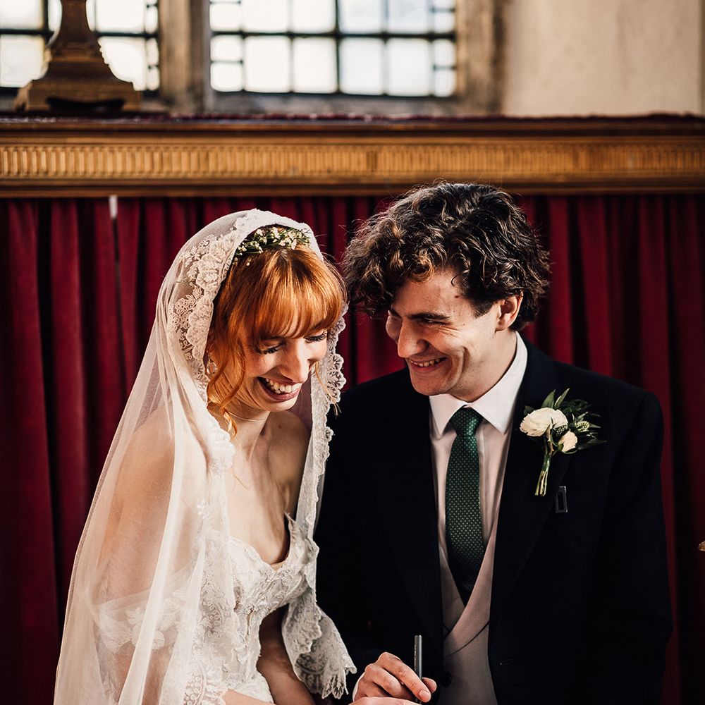 Bride and groom laugh as they sign the wedding register