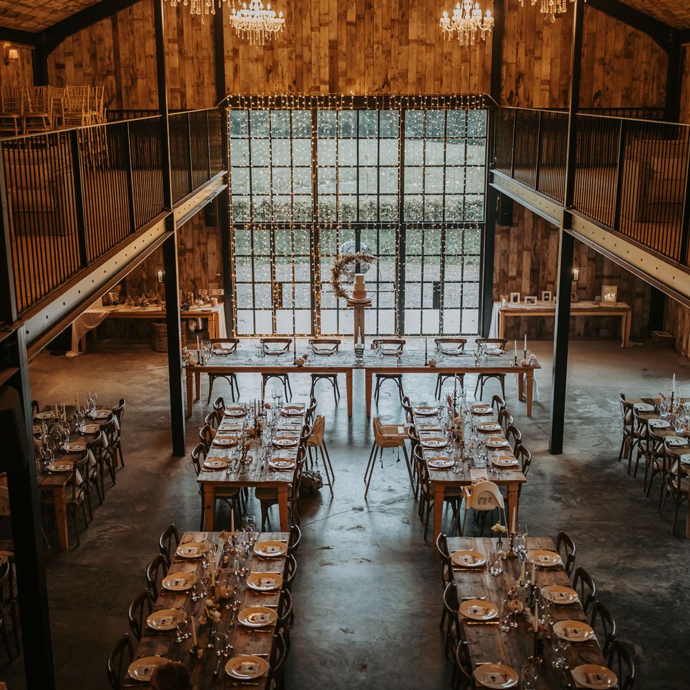 Interior of rustic barn wedding reception at Hidden River Barn with wooden wedding tables and fairy light curtain