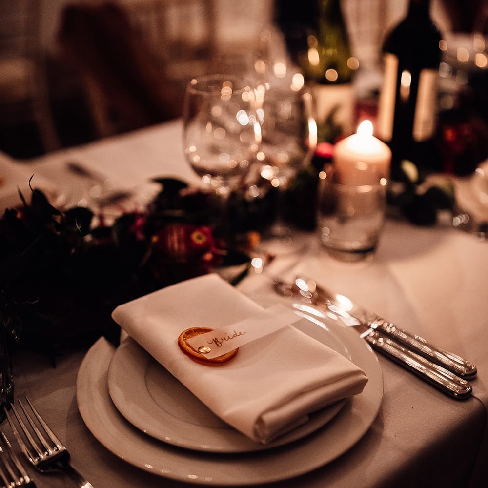 Table mat placing with white napkin, pillar candles & dried oranges on name cards 