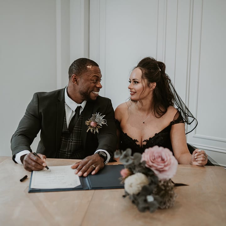 Bride & groom look lovingly at one another whilst signing marriage certificate 
