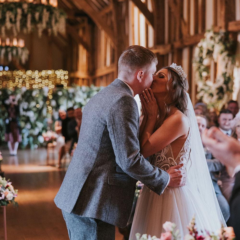 Bride and groom share their first kiss as a married couple in front of wedding guests in rustic wedding venue