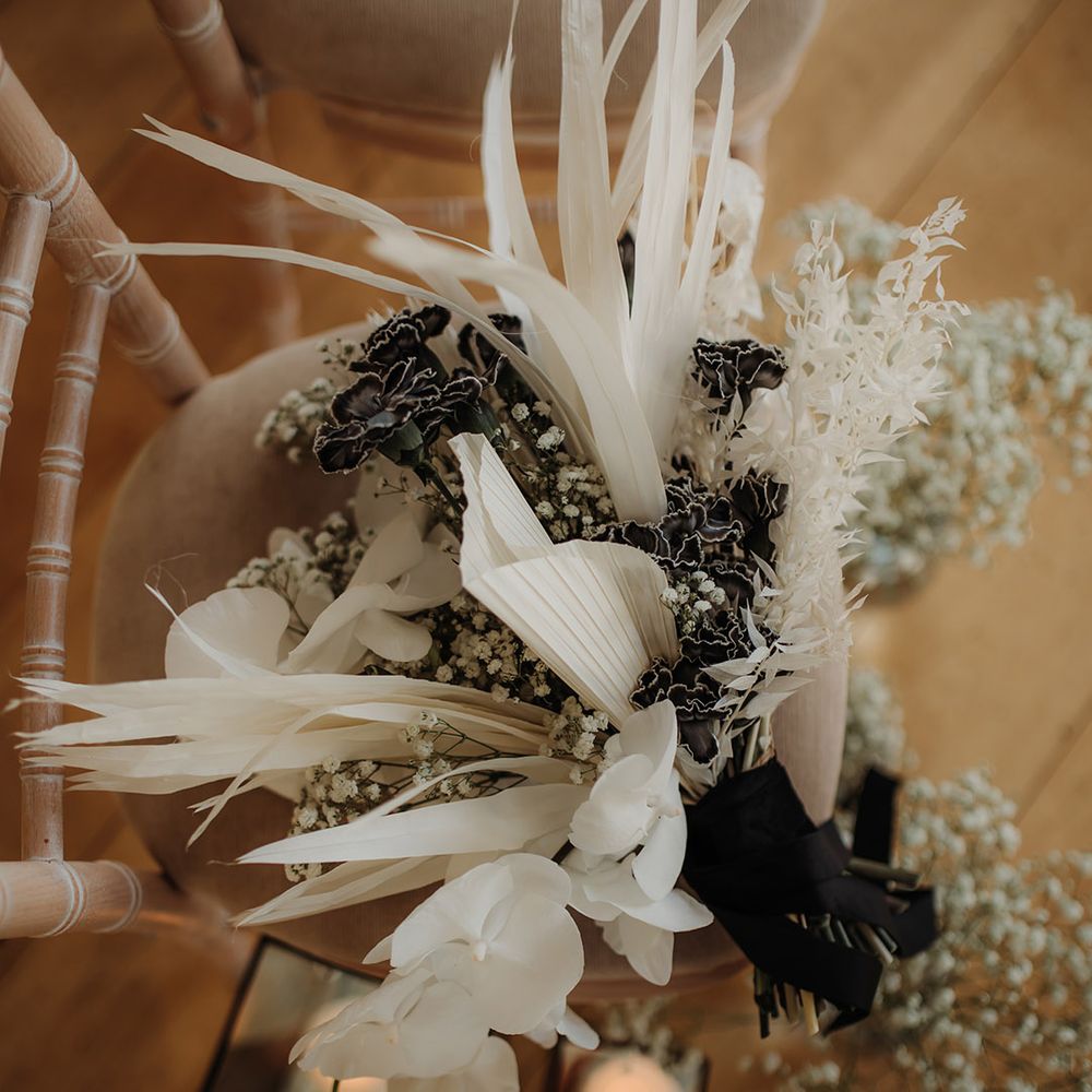 white grasses, orchids and palm leaves wedding bouquet tied with black ribbon