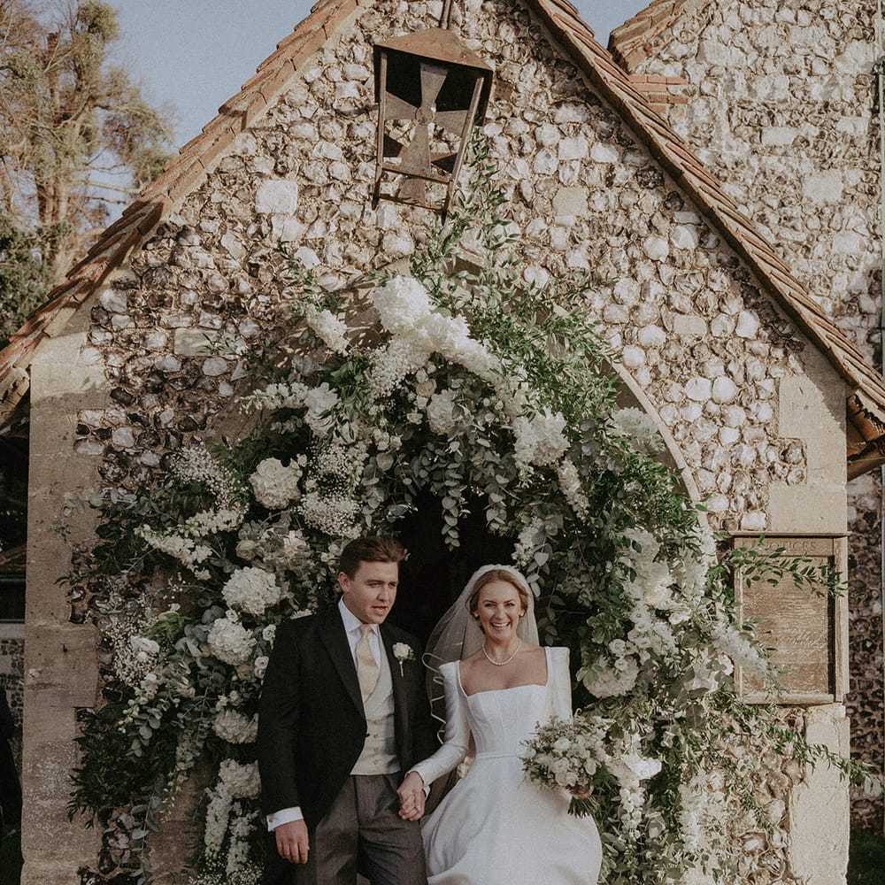 Bride and groom under large white mixed floral arch at Hedsor House wedding