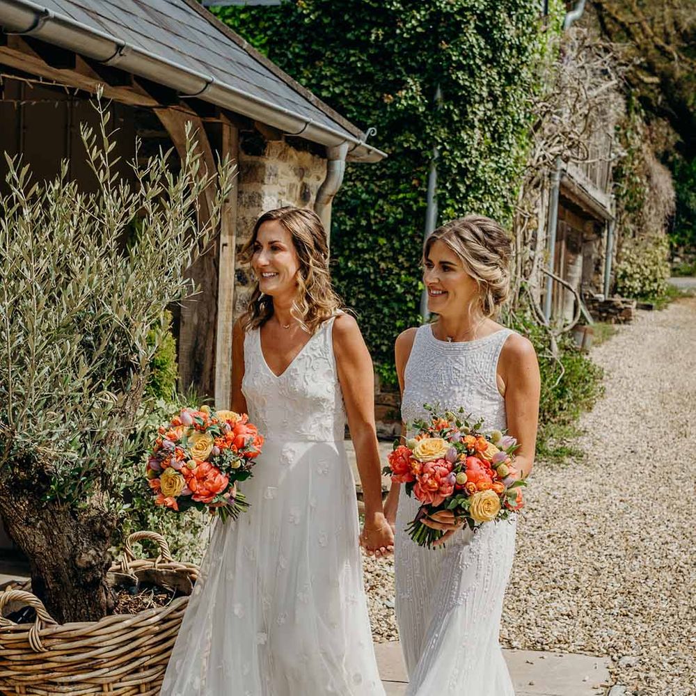 Lesbian wedding at Ever After wedding venue with two brides in lace and tulle wedding dresses holding coral peony and yellow rose wedding bouquets 