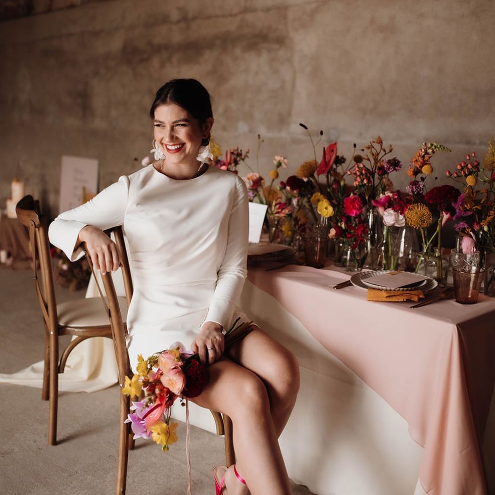 Stylish bride in a short wedding dress with fluffy pink wedding shoes sitting at her reception table 
