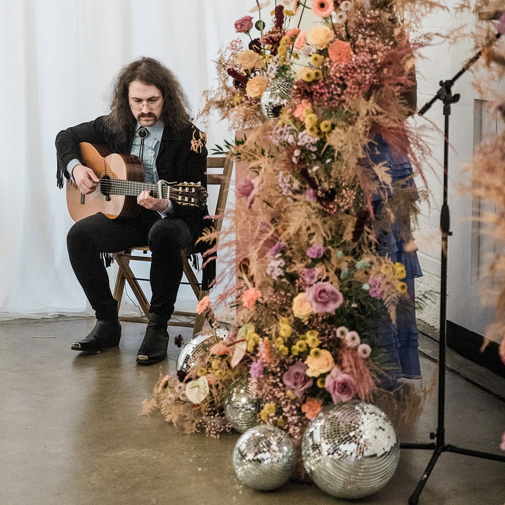Guitar player plays during the wedding ceremony with flower columns and disco balls for altar decoration 
