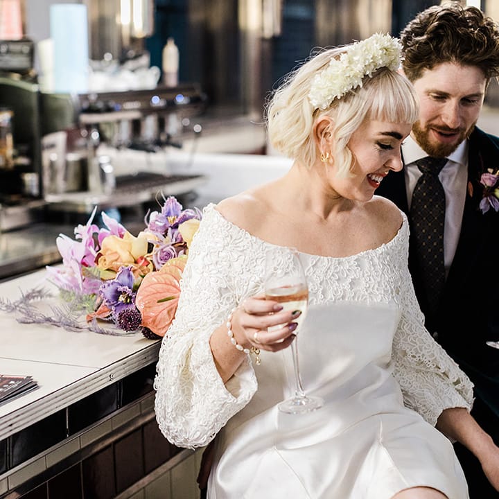 Bride and groom have a drink seated at a bar together with bouquet resting on the bar