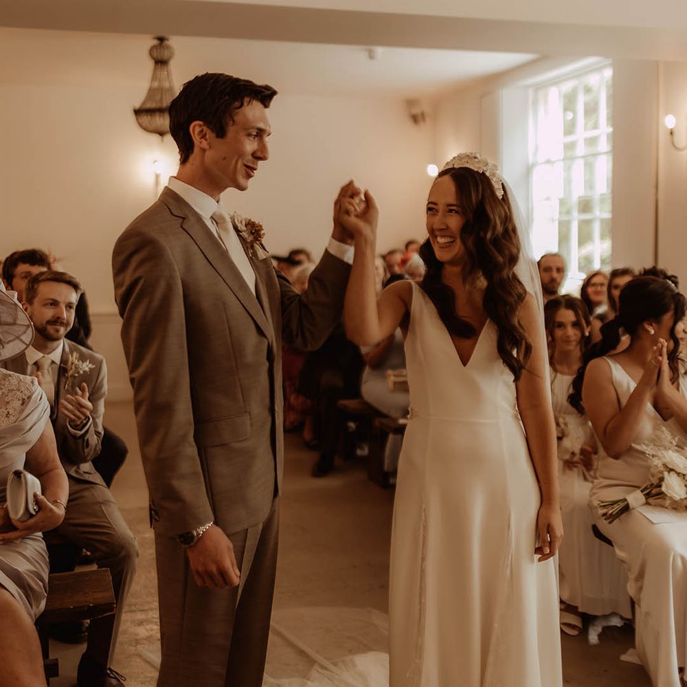 Bride and groom smile at each other as they raise their arms after getting married at Aswarby Rectory