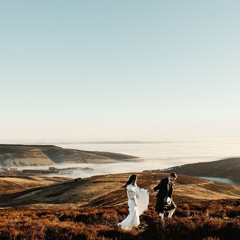 Bride & groom walk across beautiful Scottish hills during sunset on their wedding day
