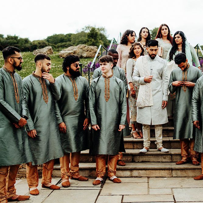 Groom stands with his groomsmen who wear traditional sherwanis with deep silver colouring, gold embellishment with gold trousers