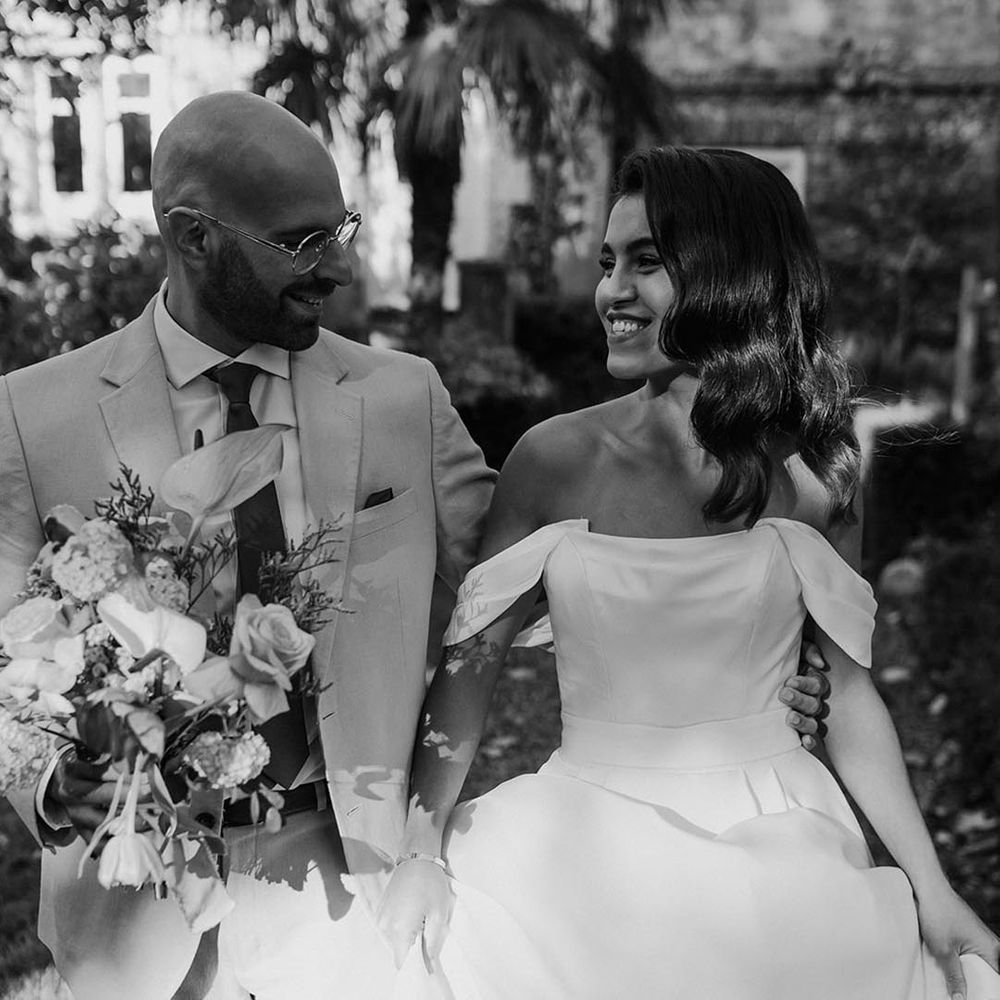Bride in a structured wedding dress with off the shoulder detail walking with the groom 