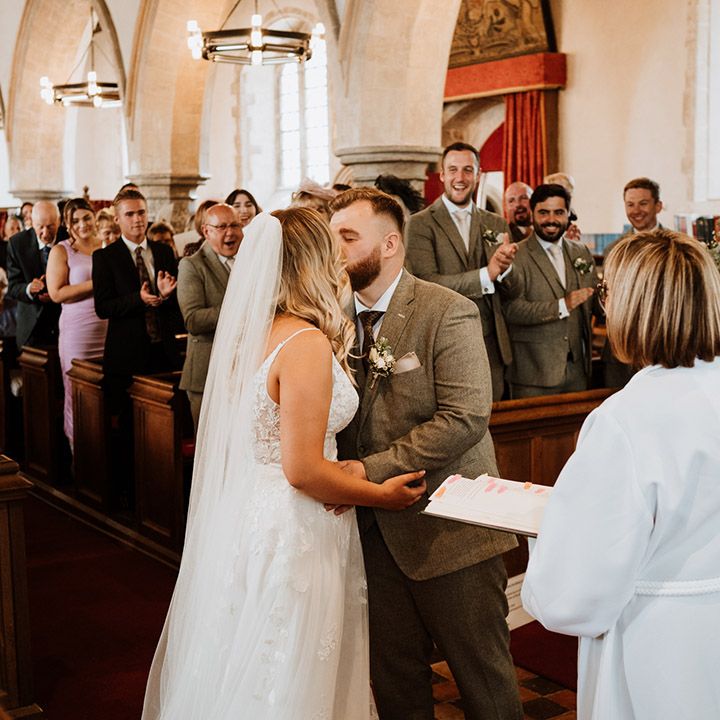 The wedding guests stand and applaud as the bride and groom share their first kiss as a married couple 