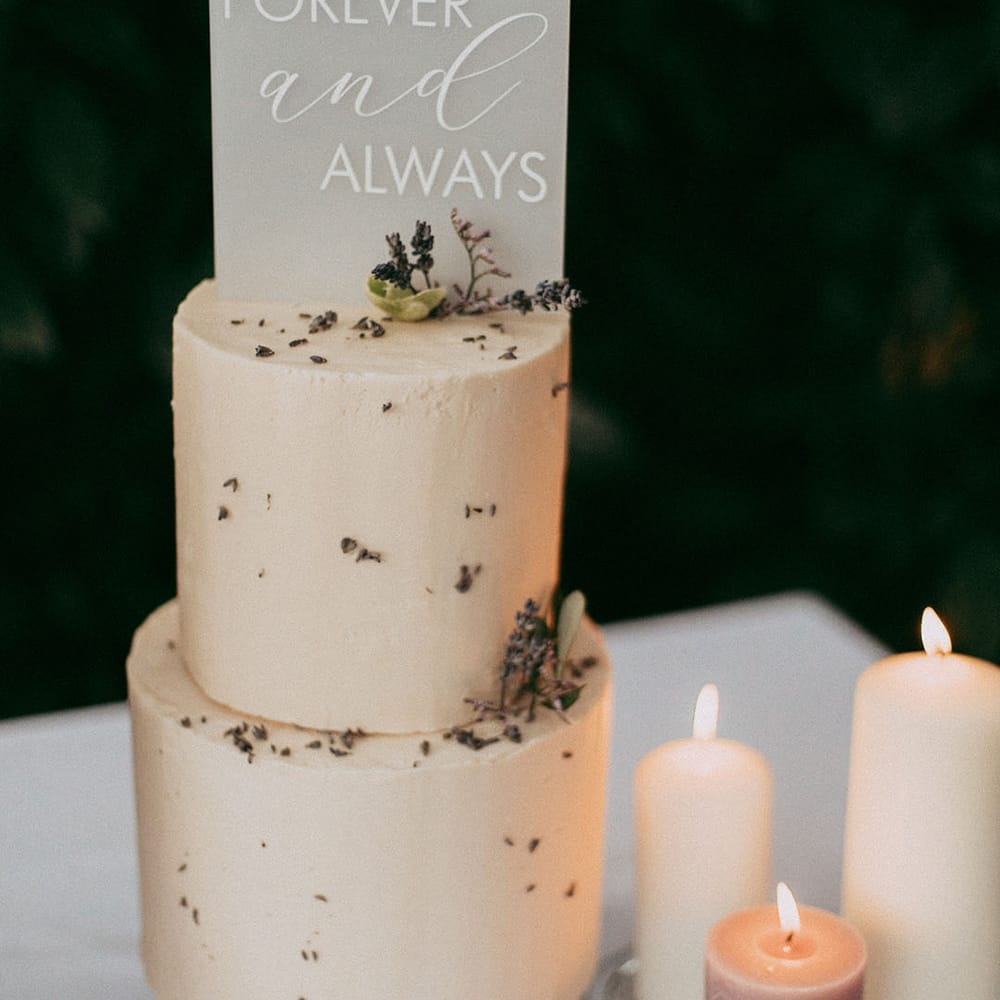 Lavender and white pillar candles with transparent engraved cake topper and two tier buttercream wedding cake with white rose and dried lavender decorations