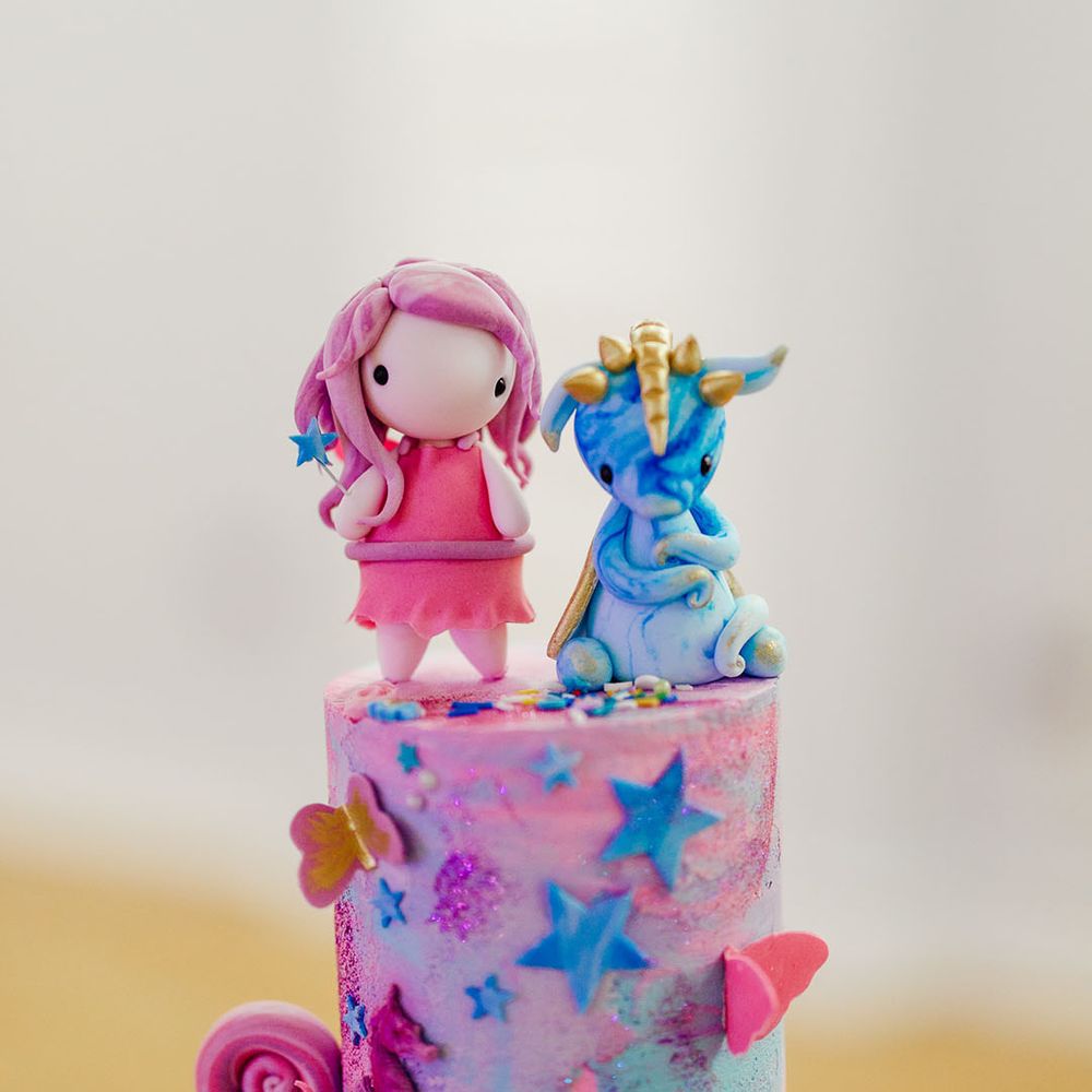 Personalised wedding cake toppers; one pink cartoon girl with pink dress and pink hair, and the other a small blue unicorn with a gold horn 